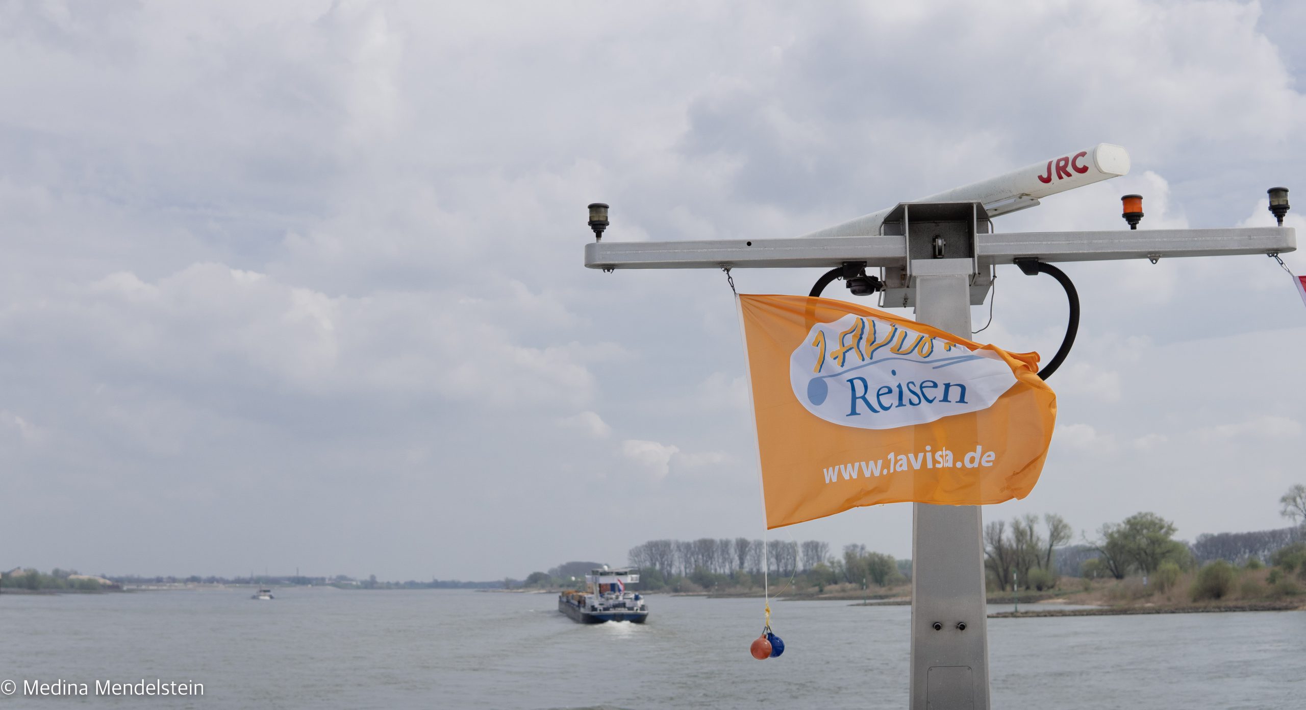 Flagge der Vista Rio von 1A Vista Reisen. Im Hintergrund der Rhein und ein Container Schiff.